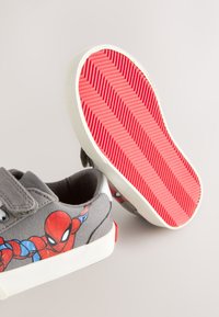 Chaussures en toile grises avec un motif Spider-Man. Elles présentent une bride à velcro, une semelle en caoutchouc blanche et un dessous rouge à motif chevrons.