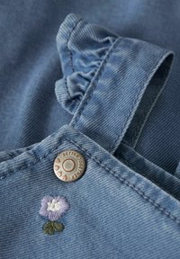 Modra denim tkanina z nabrano naramnico, kovinskim gumbom z napisom "Better Together" in detajlom cvetlične vezenine.