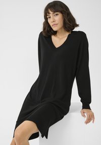 Schwarzes langärmliges Kleid mit V-Ausschnitt, aus weichem Material gefertigt, das einen lässigen Schnitt und seitliche Schlitze am Saum für Bewegungsfreiheit bietet.