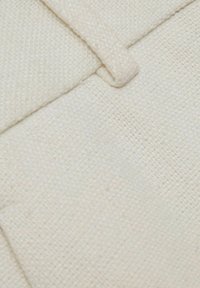 Tessuto color crema con una tessitura testurizzata, caratterizzato da un bordo piegato e un dettaglio a linguetta sottile. La superficie appare leggermente ruvida.