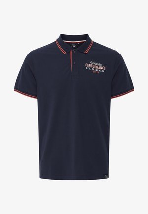 Marineblå polo-skjorte med rødstripet krage, korte ermer og brodert "Authentic PERFORMANCE" på brystet. Laget av en blanding av bomull.