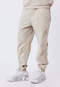 Pantalones cargo beige con puños elásticos, combinados con zapatillas Nike blancas que cuentan con suelas distintivas similares a resortes.