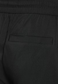 Schwarze, leichte Stoffhosen mit einem elastischen Bund und einer einfach genähten Gesäßtasche. Glatte Textur mit matter Oberfläche.