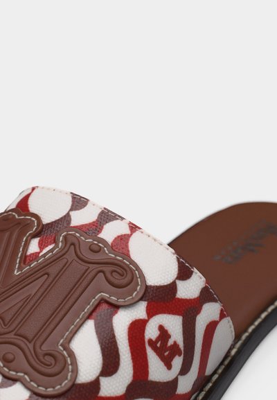 Κοντινό πλάνο κόκκινης, λευκής και καφέ διακοσμημένης σαγιονάρας με μεγάλο διακοσμητικό καφέ έμβλημα στο λουρί και ορατή ραφή.