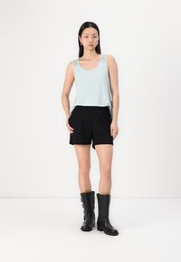 Haut sans manches bleu clair avec des détails en dentelle sur les épaules, associé à un short noir. Le mannequin porte des bottes noires jusqu'aux genoux avec des boucles.