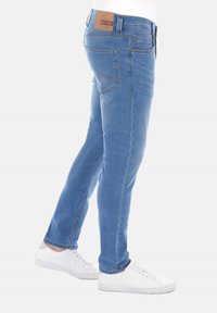 Vaqueros de denim azul claro con corte ajustado, que presentan un parche de cuero en la cinturilla y costuras sutiles en los bolsillos traseros.