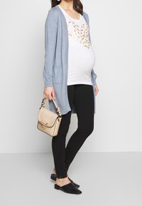 Světle modrý cardigan, bílá tričko s potiskem zlatého motýla, černé legíny, černé mokasíny a strukturovaná béžová kabelka.