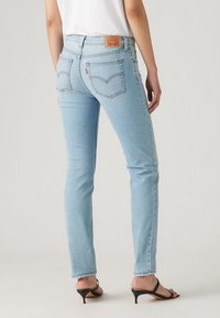 Jeans de mezclilla azul claro con un corte ajustado, cintura de altura media y un destacado detalle en los bolsillos. Presentan un parche de marca en la parte trasera y un dobladillo deshilachado.