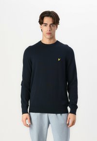Maglione lavorato a maglia blu navy con collo rotondo, maniche lunghe e polsini a coste. Presenta un piccolo logo giallo sul lato sinistro del petto.