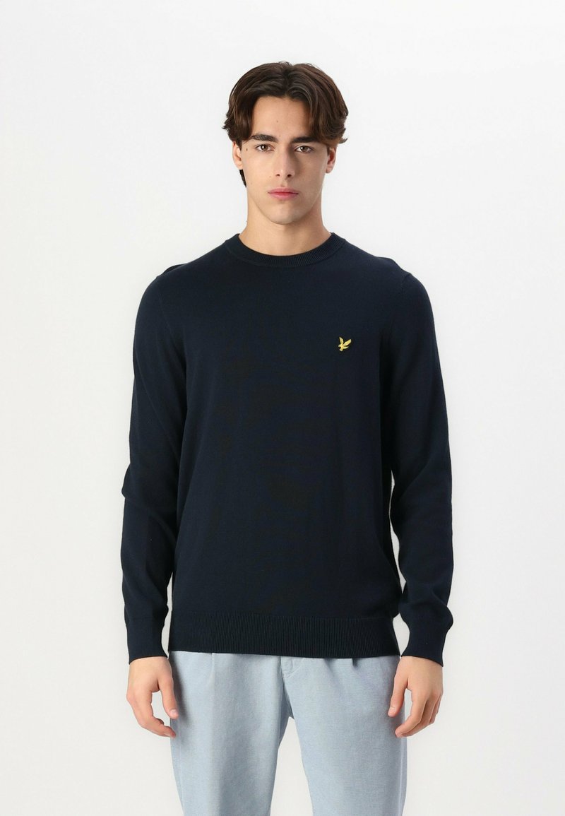 Maglione lavorato a maglia blu navy con collo rotondo, maniche lunghe e polsini a coste. Presenta un piccolo logo giallo sul lato sinistro del petto.