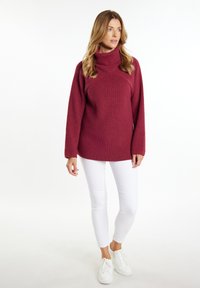 Bordeaux gebreide trui met hoge col en lange mouwen, gecombineerd met witte strakke broek en witte sneakers. Zachte textuur, ontspannen pasvorm.