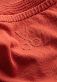 Rode T-shirt met korte mouwen, voorzien van een subtiel geborduurd logo van scharen. De stof lijkt zacht met een geribbelde halslijn.