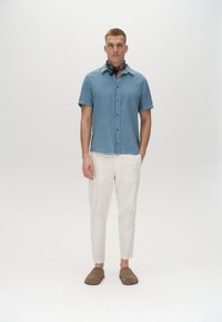 Ko�šela na krátky rukáv, svetlomodrá, s textúrovaným povrchom, v kombinácii s krémovými nohavicami a hnedými slip-on topánkami. Čierny šál s vzorom okolo krku.