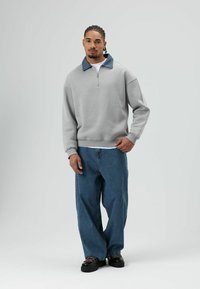 Grijze zip-up sweatshirt met een denim kraag, gecombineerd met losse blauwe jeans en zwarte schoenen met gestructureerde zolen. Eenvoudig en functioneel ontwerp.