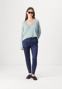 Světle modrý croptop svetr s výstřihem do V, v kombinaci s námořnickými kalhotami na míru a černými slip-on botami. Modelka má na sobě přehnané sluneční brýle.