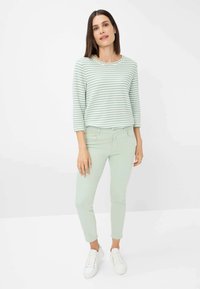 Maglietta a maniche lunghe a righe verde menta e pantaloni attillati abbinati, indossati con scarpe da ginnastica bianche, su uno sfondo bianco semplice.