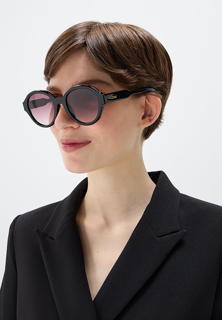 Runde Sonnenbrillen mit schwarzen Rahmen und gradienten rosafarbenen Linsen. Sie besitzen ein elegantes Design und ein Logo am Bügel. Tragen Sie sie mit einem schwarzen Blazer.