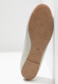 Semelle d'une chaussure blanche avec une semelle en caoutchouc marron présentant des motifs paisley et en forme de cœur ainsi que l'inscription de la taille 37.