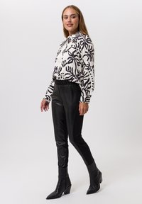 Black and white floral-patterned blouse with long sleeves, paired with glossy black fitted pants and pointed-toe black ankle boots.