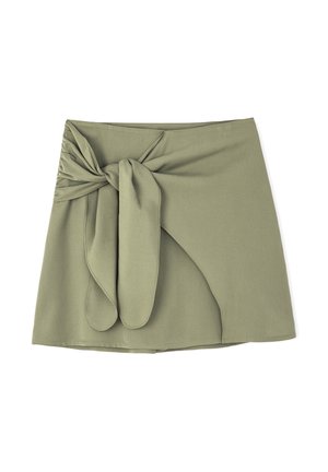 Mini-jupe vert olive en tissu doux, avec un détail de nœud à l'avant et un ourlet légèrement asymétrique, présentant une texture lisse.