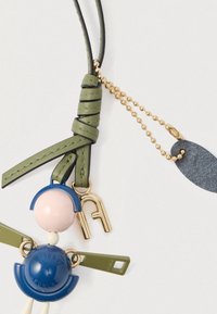 Farebná kľúčenka s modrým a ružovým motívom, zelenými koženými detailmi, zlatou kovovou výbavou a okrúhlym tvarom s textúrovaným povrchom.