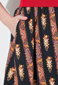 Schwarze Bleistiftskirt mit floralem Paisley-Muster in Orange, Rosa und Gelb. Mit einem gerafften Taillenbund und seitlichen Taschen für Funktionalität.
