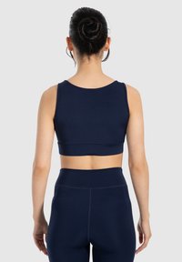 Marineblauwe sportcrop top met een ronde halslijn, brede banden en een soepele pasvorm. Draag het met bijpassende high-waisted leggings.