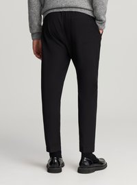 Pantaloni neri dalla vestibilità comoda, con vita elastica e due tasche posteriori. Indossati con scarpe nere e maglione grigio. Design semplice e pulito.