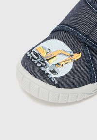 Mörkblå denimskor med vit gummisula. Har broderad konstruktionfordon och logotypdetalj på tån. Stängning med verstelås.