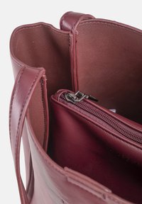 Maroon leather tote bag with an open top, featuring an inner zippered compartment with silver hardware, smooth texture, and durable design.