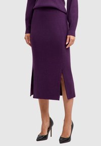 Gebreide paarse rok met zijsplitten, ontworpen met een aansluitende silhouet. Gecombineerd met zwart gestructureerde hoge hakken.