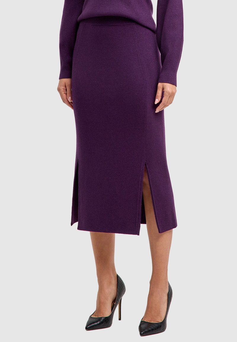 Gebreide paarse rok met zijsplitten, ontworpen met een aansluitende silhouet. Gecombineerd met zwart gestructureerde hoge hakken.