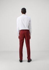 Fehér, hosszú ujjú ing fekete gombokkal, piros nadrággal párosítva; sima textúrájú és slim fit kivitelezés, hátulról nézve, fekete cipőkkel.