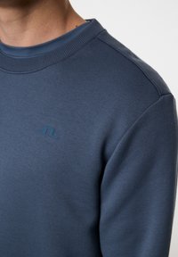 Sininen huppari, jossa on pyöreä kaulus, ribbikuvioitu kaulus ja minimalistinen logo rinnassa. Smooth texture ja istuva muotoilu.