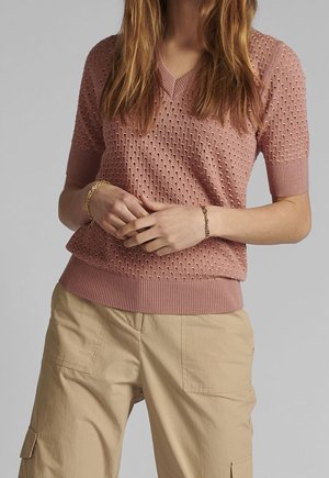Pull court à manches courtes en tricot rose clair avec col en V, motif texturé et ourlets côtelés, assorti à un pantalon cargo beige.