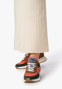 Mehrfarbige Sneakers mit orangefarbenem und grünem Wildleder, Akzenten im Leopardenmuster, weißen Schnürsenkeln und einer dicke weißen Außensohle mit gelben Details.