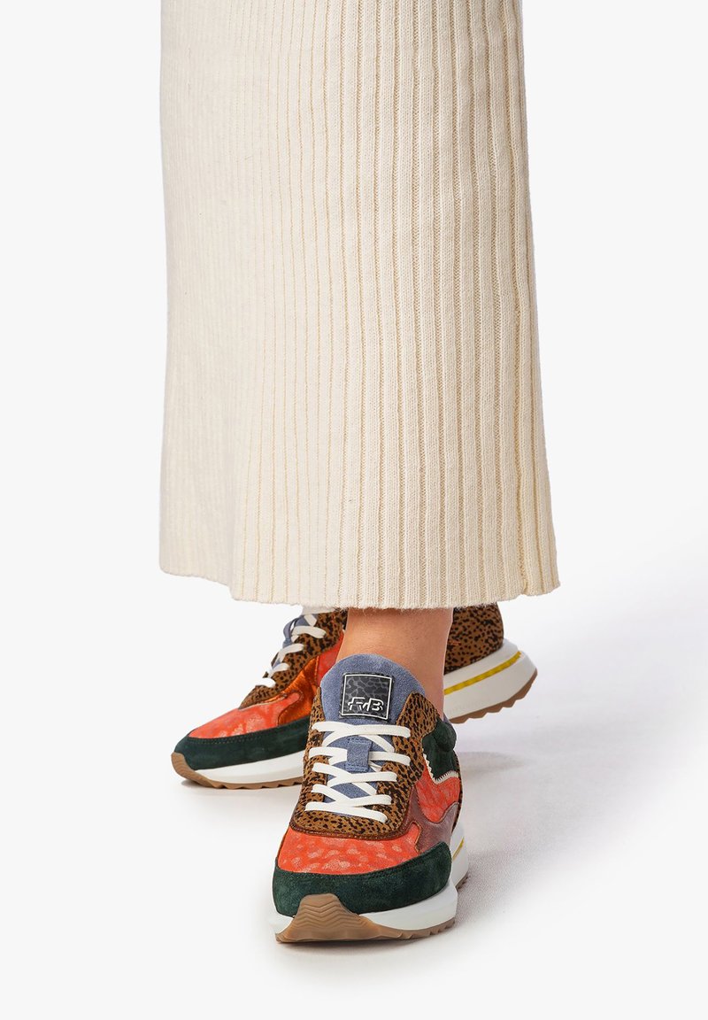 Mehrfarbige Sneakers mit orangefarbenem und grünem Wildleder, Akzenten im Leopardenmuster, weißen Schnürsenkeln und einer dicke weißen Außensohle mit gelben Details.