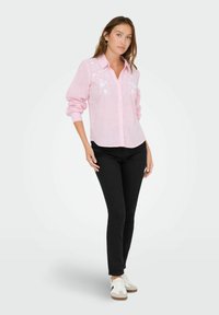 Camicia a righe rosa con ricami floreali sul petto, abbinata a jeans skinny neri e sneaker bianche.
