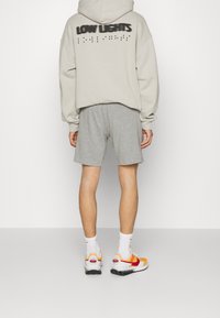 Béžová mikina s kapucí, na zadní straně s potiskem "LOW LIGHTS" v černé barvě, v kombinaci se šedými šortkami a vícebarevnými teniskami. Viditelné bílé ponožky.