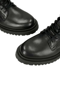 Stivaletti in pelle nera con texture liscia, punta rotonda e suola in gomma spessa. Presentano occhielli per i lacci e dettagli cuciti.