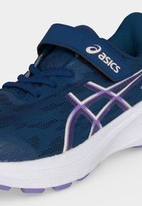 Μπλε παιδικό αθλητικό παπούτσι Asics με μωβ και λευκές λεπτομέρειες, λουράκι με βέλκρο, κορδόνια και μαλακή λευκή σόλα με μωβ πέλμα.
