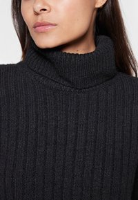 Schwarzer Rollkragenpullover mit geripptem Muster. Der Stoff wirkt dick und weich, hat einen hohen Kragen und dezente Nähte.