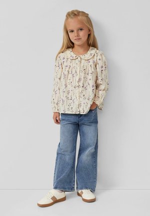 Langarmige, crèmekleurige blouse met bloemenpatroon en ronde kraag, gecombineerd met lichtblauwe wijde jeans en witte sneakers met bruine accenten.