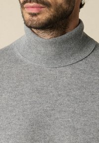 Maglione grigio a collo alto con texture a costine e design aderente. Primo piano del colletto e della parte superiore del torace, superficie del tessuto liscia.