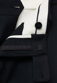 Black fabric jacket with a white inner collar, featuring a black button, contrasting stitching, and a zippered pocket detail on the inside.