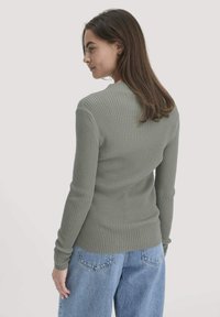 Rippstrickpullover in Grün mit langen Ärmeln, runden Ausschnitt und taillierter Form, kombiniert mit blauen, lässigen Denim-Jeans.