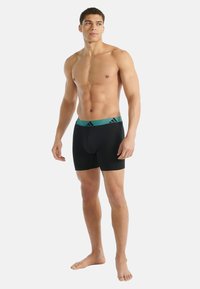 Czarne bokserki z turkusową elastyczną talią ozdobioną trzema czarnymi paskami. Tkanina wygląda na gładką i dopasowaną.