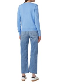 Lichtblauwe trui met lange mouwen, gecombineerd met hoge taille lichte denim jeans. Witte sneakers met zwarte accenten maken de outfit af.
