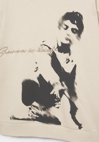 Schita monocromă a unei persoane așezate cu un genunchi ridicat, purtând haine casual, cu un text cursiv parțial vizibil pe țesătură.