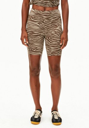 Persoon die bruine en beige zebra-print biker shorts en een bijpassende top draagt, gecombineerd met zwarte sneakers met beige veters en rubberen zolen.